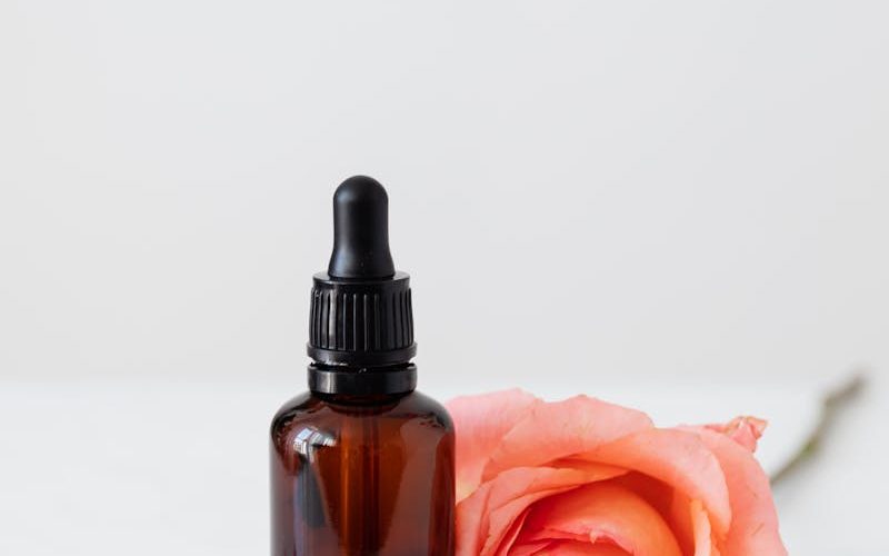 Elegant dropper bottle with pink rose petals on a wooden plate, perfect for aromatherapy or skincare.