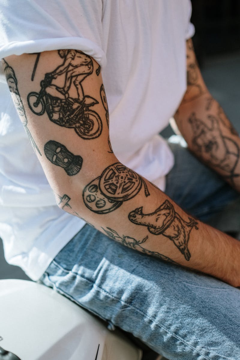 A detailed shot of a tattooed arm wearing a white shirt and denim pants, showcasing unique designs.