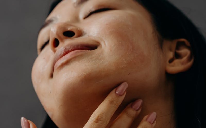 Woman enjoying a facial massage with closed eyes and relaxed expression, promoting self-care and wellness.